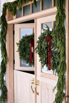 the front door is decorated for christmas with evergreen wreaths and red ribbon on it