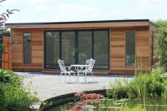 a garden room with chairs and table next to a small pond in front of it