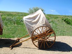 an old fashioned covered wagon sitting on top of a dirt road next to a field