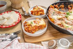 a wooden table topped with plates and bowls filled with lasagna casserole