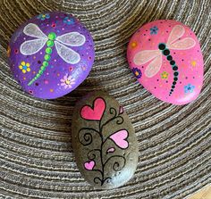 three painted rocks with dragonflies and hearts on them sitting on a wicker surface