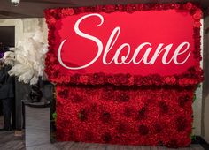 a red sign that says sloane surrounded by white feathers and other people in the background