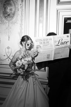 a bride and groom are reading the paper together in their wedding day attire, with sunglasses on