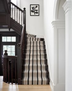 a stair case with black and white striped carpet next to a wooden banister in a home