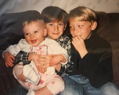 three children sitting on a couch with their arms around each other