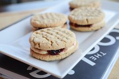 three cookies with jelly filling on a white plate next to a black and white book