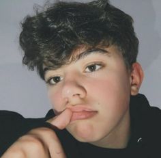 a young boy with his finger in his mouth looking at the camera while wearing a black shirt