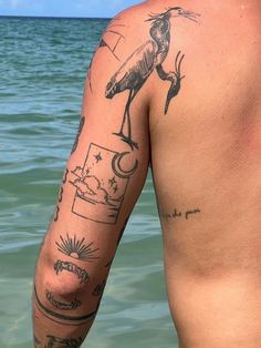 a man standing in the water with tattoos on his arm and shoulder, looking at the ocean