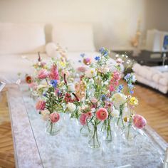 flowers are arranged in vases sitting on a glass table with white furnishing