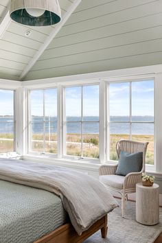 a bedroom with a bed, chair and large windows overlooking the beach in front of it