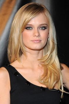 a woman with blonde hair and blue eyes posing in front of a black background wearing a black dress