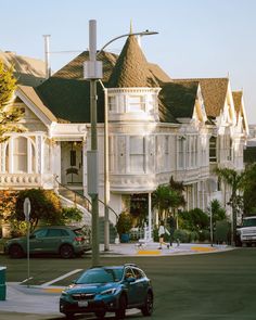 two cars are parked on the street in front of some white victorian style houses with brown roof tops