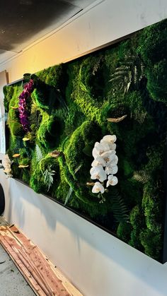 a large moss covered wall with flowers and plants on it's side in a building