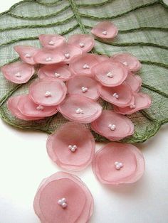 some pink flowers are sitting on top of a green lace table cloth with pearls in the center