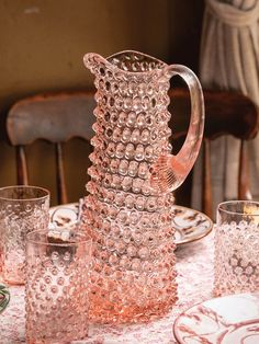 a pink glass pitcher sitting on top of a table next to glasses and plateware