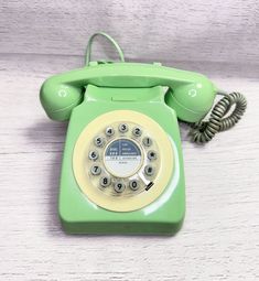 an old fashioned green phone sitting on top of a white wooden table next to a telephone cord