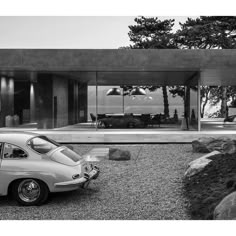 an old car is parked in front of a modern house with glass walls and doors