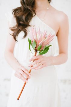 a woman in a white dress holding a pink flower with green leaves on her arm