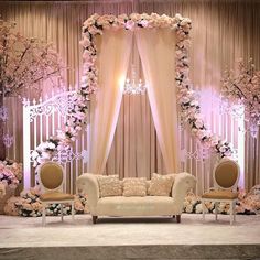 a couch and two chairs in front of a stage decorated with flowers