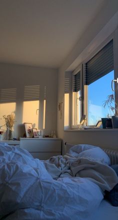 an unmade bed sitting in front of a window with the sun shining through it