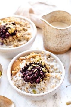 three bowls filled with oatmeal and fruit on top of a white table