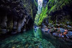 a man is wading through a narrow river in the middle of a mountain gorge