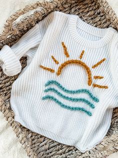 a knitted sweater with the sun and water on it sitting in a wicker basket