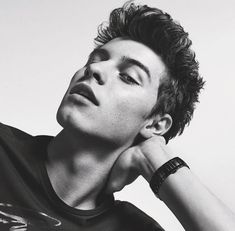 a black and white photo of a young man with his hand on his head looking up