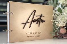 a wedding guest book with the name and date engraved on it next to a bouquet of flowers