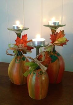 three pumpkin shaped candles are sitting in vases with leaves and ribbons on the sides