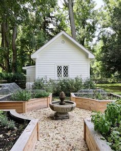 a small white house surrounded by lots of trees and plants with a fountain in the middle