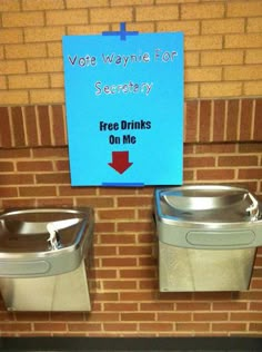 two metal urinals sitting on top of a brick wall next to a sign