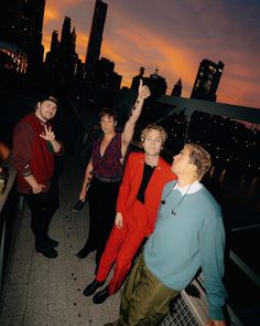 four people are standing on a bridge with their arms in the air and one person is holding up a cell phone