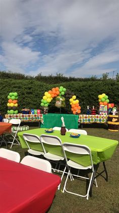 tables and chairs are set up in the grass for an outdoor party with colorful balloons