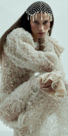 a woman with long hair wearing a white dress and beaded headpiece, standing in front of a white background