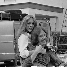 a woman sitting on the back of a man's lap in front of a van