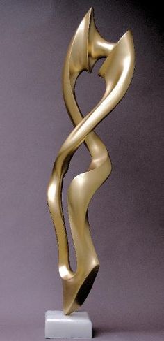 a gold sculpture sitting on top of a white pedestal in front of a gray wall