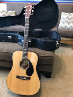 an acoustic guitar sitting on the floor next to a couch with a case in it