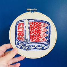 a hand is holding up a small embroidery hoop with red and blue designs on it