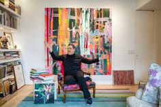 a man sitting on a chair in front of a colorful painting and bookshelf