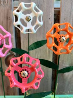 four different colored flower shaped objects in front of a wooden fence with green leaves on it