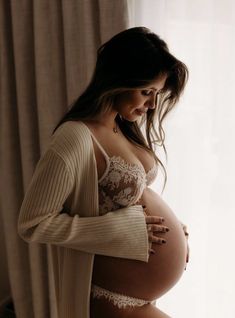 a pregnant woman is standing in front of a window with her hands on her belly