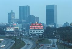 the city skyline is lit up in red and white as cars drive down the road