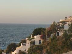 an ocean view with white buildings and trees on the hillside next to the water's edge