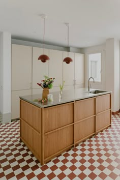 a kitchen with checkered flooring and an island in the middle is seen from across the room