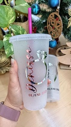 a person holding up a plastic cup in front of a christmas tree with the words happy on it