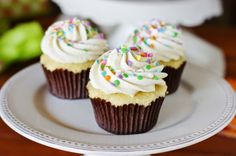 three cupcakes with white frosting and sprinkles on a plate