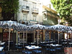 an outdoor dining area with tables and umbrellas in front of a building on a city street