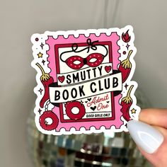 a person holding up a sticker with the words smutty book club on it