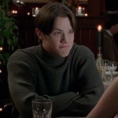 a woman sitting at a table with a glass in front of her and candles on the wall behind her